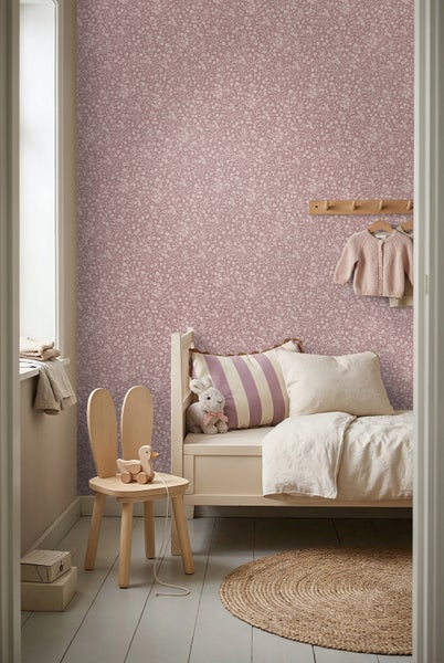 Hell eingerichtetes Kinderzimmer mit floral gemusterter Tapete, einem weißen Holzbett, einem runden Jute-Teppich und einem Stuhl in Hasenform.