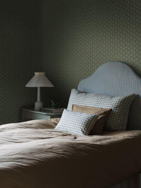 Schlafzimmer mit Bett, Nachttisch und Lampe vor gemusterter Tapete