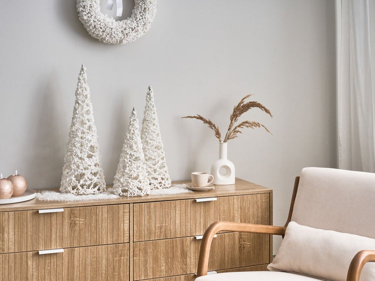 Weihnachtliche Dekoration mit Dekobäumen, Kranz, Kerzen und Trockenblumen auf einer Kommode