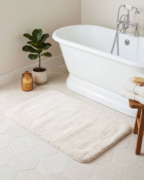 Rechteckiger Badteppich in einem Badezimmer mit Badewanne, Zimmerpflanze und Holzhocker auf einem Fliesenboden mit Hexagonmuster