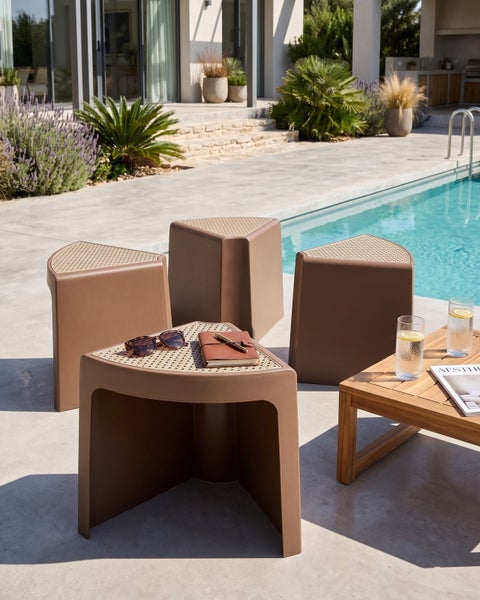 Vier braune dreieckige Outdoor-Hocker mit Geflecht-Oberfläche auf einer hellen, modernen Terrasse am Pool im organisierten Lounge-Stil.