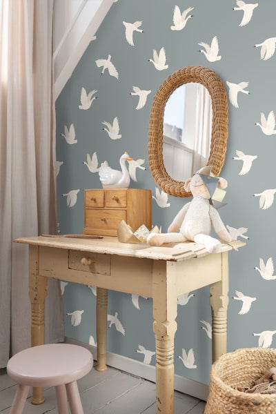 Kinderzimmer Szene mit Holztisch, Hocker, Spiegel und Schrank vor einer Tapete mit Vogelmuster