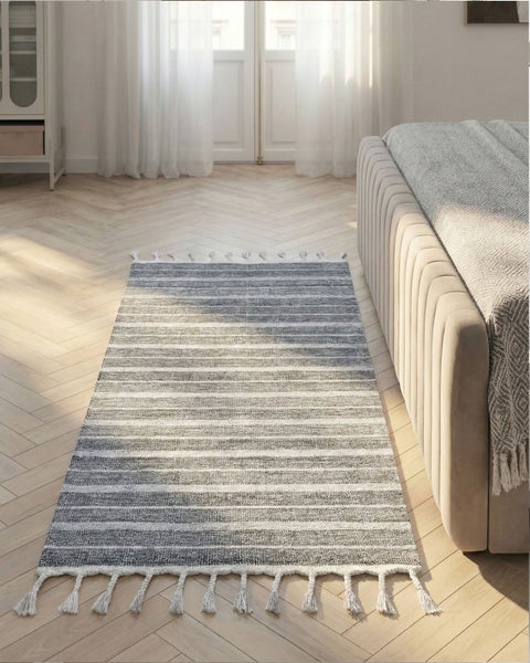 Gestreifter Läufer mit Fransen auf hellem Fischgrätparkett in einem hellen, modern eingerichteten Zimmer neben einem Polsterbett.