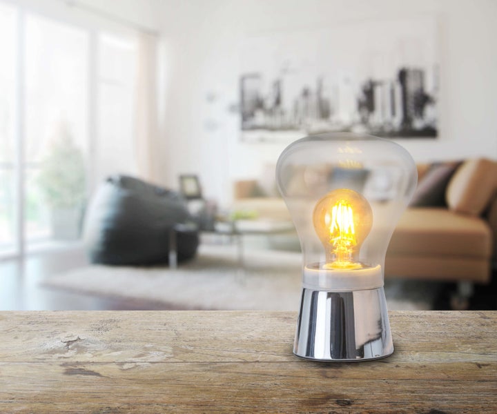 Dekorative Lampe in Glühbirnenform auf Holztisch vor hellem Wohnzimmerhintergrund.