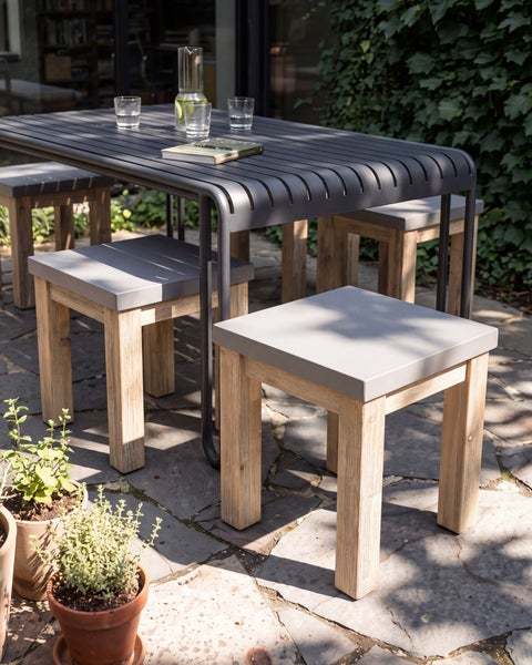 Gartentisch mit vier Hockern aus Holz und Metall auf einer Terrasse mit Topfpflanzen.