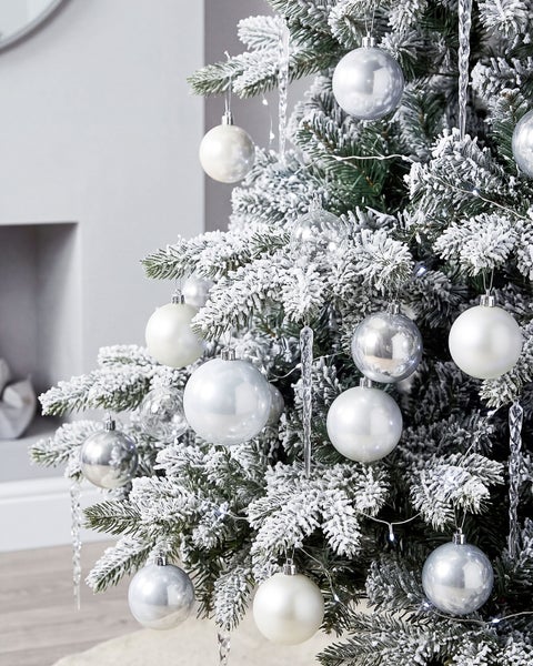 Künstlicher Weihnachtsbaum mit künstlich beschneiten Zweigen, geschmückt mit verschiedenen glänzenden und matten Kugeln sowie Eiszapfen.