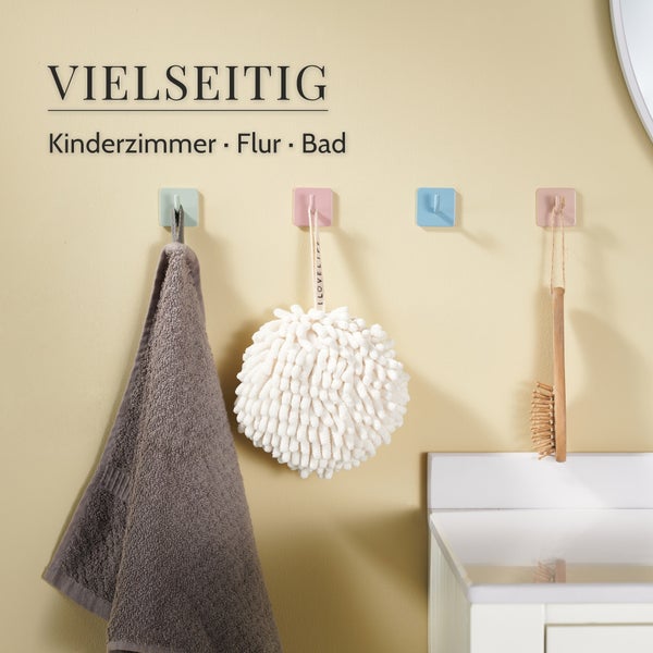 Vier quadratische Wandhaken in verschiedenen Pastelltönen montiert an einer Wand, verwendet für Handtuch, Duschschwamm und Holzbürste.