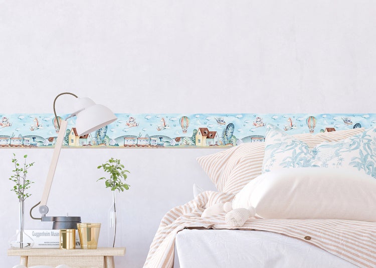 Helles Kinderzimmer mit selbstklebender Wandbordüre an einer weißen Wand. Motive: Tiere in Flugzeugen, ein Zug und Häuser. Mit Bett und Nachttisch.