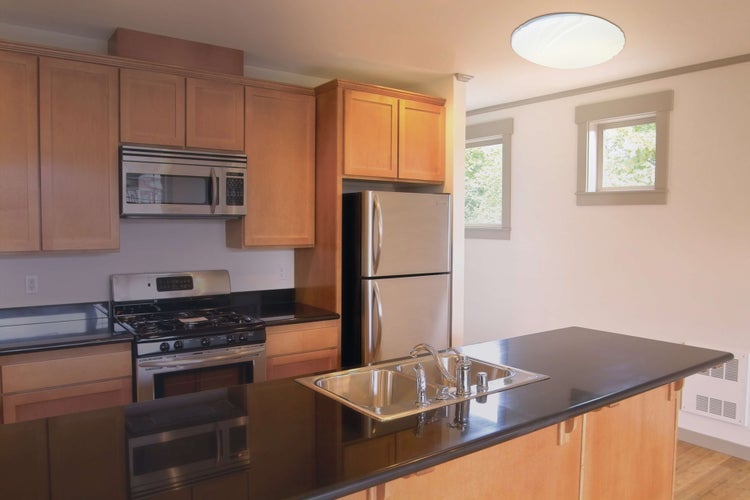 Helle Küche mit Edelstahlgeräten, Spüle in Arbeitsplatte integriert und Holzschränken