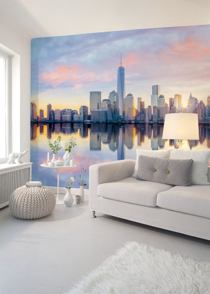 Modernes Wohnzimmer mit weißem Sofa, hellem Strickhocker und Fototapete der Skyline von New York City bei Sonnenuntergang.