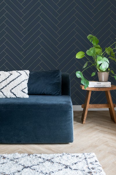 Wohnzimmer mit Sofa, Kissen, Pflanze und Wandtapete im Fischgrätmuster