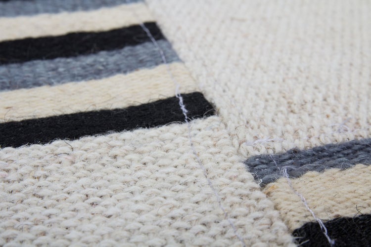 Nahaufnahme eines gewebten Wollteppichs mit Streifenmuster in Schwarz, Grau und Beige.
