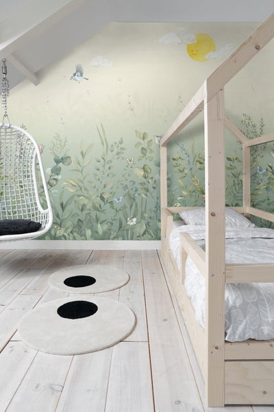 Helles Kinderzimmer mit Holzbett, Schaukelstuhl, runden Teppichen und botanischer Tapete