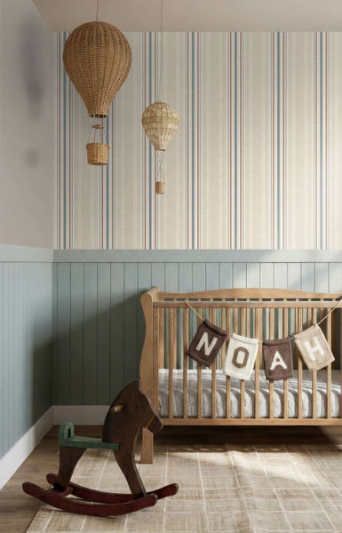 Kinderzimmer mit gestreifter Tapete, hängenden Heißluftballon-Dekoartikeln aus Rattan, Gitterbett und hölzernem Schaukelpferd auf dem Boden.