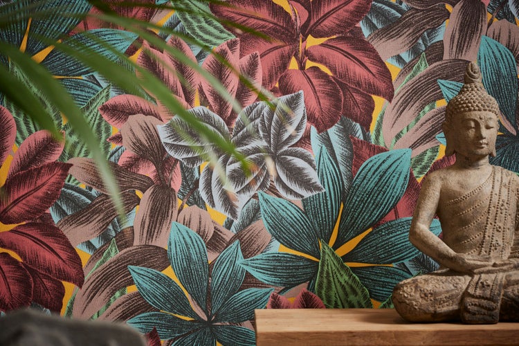 Wohnraum mit floral gemusterter Tapete, Buddhaskulptur, Dekorationselementen und einer Frau in gehäkeltem Kleid.