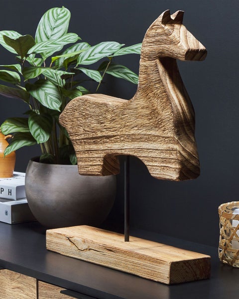 Dekorative Holzpferdfigur auf Ständer neben einer Zimmerpflanze