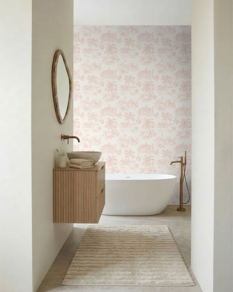 Helles Badezimmer mit freistehender Badewanne, hängendem Waschbeckenunterschrank aus Holz, Steinwaschbecken, ovalem Spiegel und gemusterter Tapete.