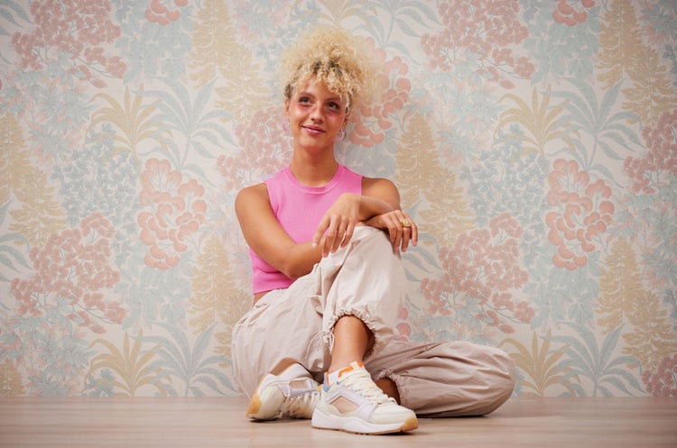 Porträt einer Frau mit rosa Oberteil vor floraler Tapete