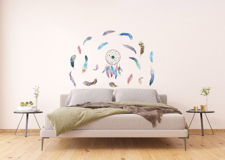 Wandtattoo mit Traumfänger und verschiedenen Federn in einem hellen Schlafzimmer über einem Bett.