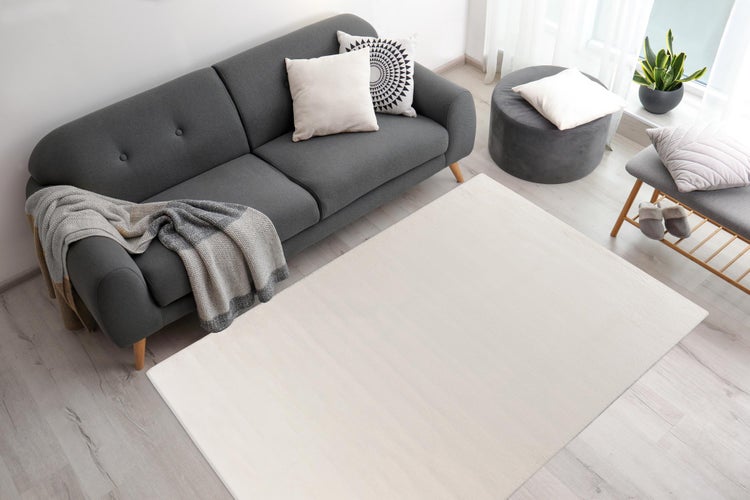 Heller, rechteckiger Teppich in einem modern eingerichteten Wohnzimmer mit grauem Sofa und hellem Boden.