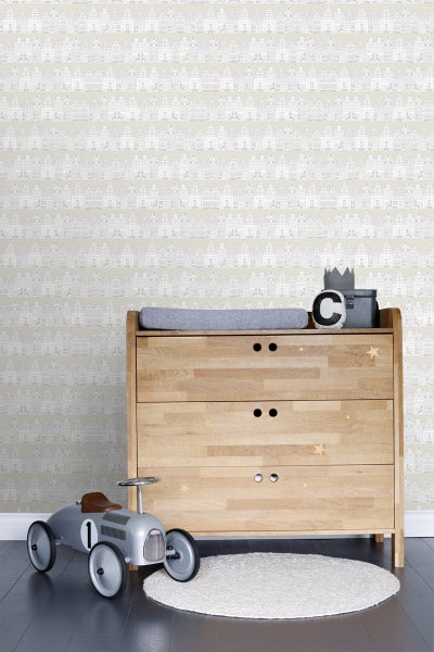 Ein Kinderzimmer mit einer Kommode aus Holz, einem Spielzeugauto und einer Tapete mit Häusermuster.
