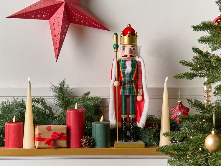 Festliche Dekoration mit Nussknacker, Sternen, Kerzen und Geschenk auf einem Kaminsims