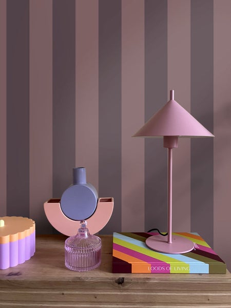 Vertikal gestreifte Vliestapete hinter einer Kommode mit einer Tischleuchte und verschiedenen dekorativen Vasen in einem modern gestalteten Innenraum.
