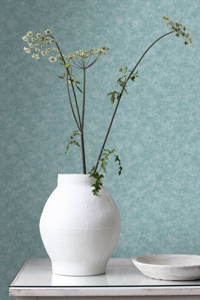 Dekorative Szene mit einer weißen Vase mit Pflanzen vor einer strukturierten Tapete