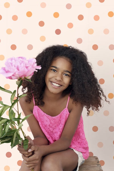 Porträt eines lächelnden Mädchens mit einer Pfingstrose vor einem gepunkteten Hintergrund.