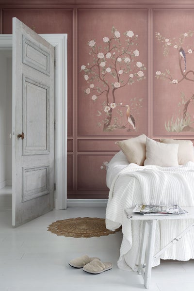 Helles Schlafzimmer mit floraler Wandtapete, geöffneter Tür und weißer Tagesdecke