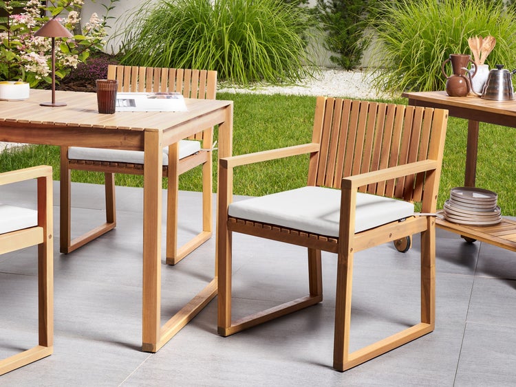 Moderne Gartenmöbel aus Holz mit rechteckigem Tisch und Stühlen mit Sitzpolstern auf einer gepflasterten Terrasse neben einer Rasenfläche.