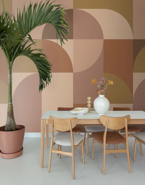 Esszimmer mit Esstisch, Stühlen, Zimmerpflanze und gemusterter Tapete.