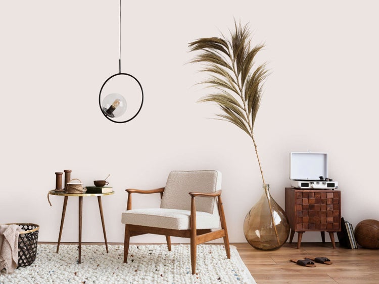 Heller Wohnraum mit Holz-Sessel, weißem Polster, rundem Beistelltisch, schwarzer Pendelleuchte, großer Glasvase mit Trockenpflanze und Plattenspieler.