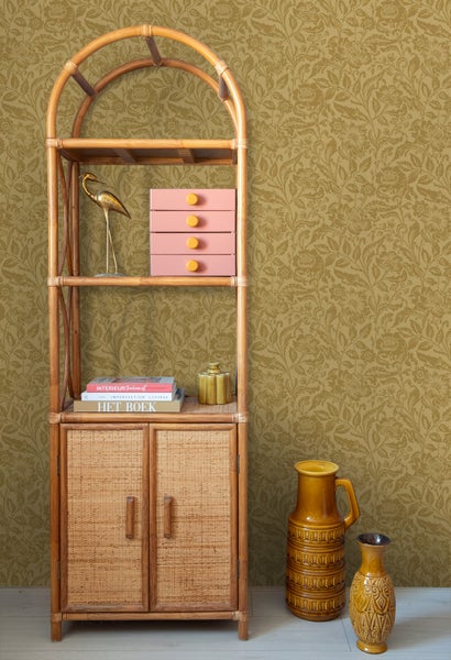 Dekorative Szene mit einem Bambusregal, einem goldenen Reiher, einer rosa Schubladenbox, Büchern und keramischen Vasen vor einer floralen Tapete