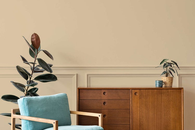 Wohnzimmer mit Wandleisten an einer beigen Wand, Sideboard aus Holz, hellblauem Sessel und Zimmerpflanzen.