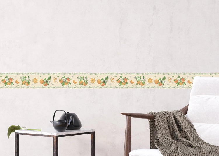 Tapetenbordüre mit Orangen- und Blättermotiv an einer hellen Wand, kombiniert mit einem modernen Sessel und Beistelltisch.
