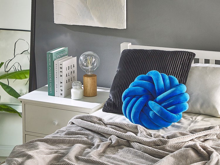 Dekoratives Schlafzimmerambiente mit Nachttisch, Lampe, Büchern, Kissen und Tagesdecke