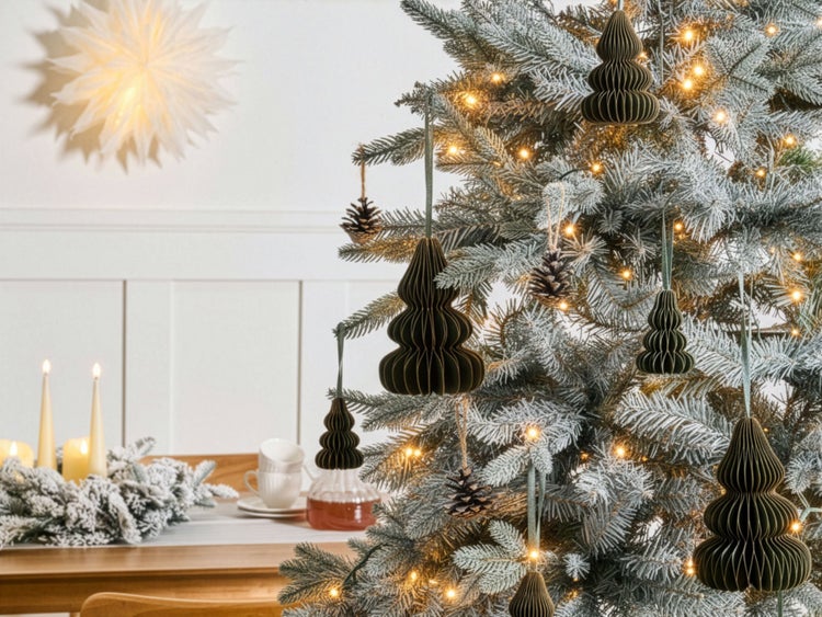 Weihnachtsbaum dekoriert mit grünen Papieranhängern in Wabenoptik, Tannenzapfen und warmweißen Lichtern in einem festlich gestalteten Raum.