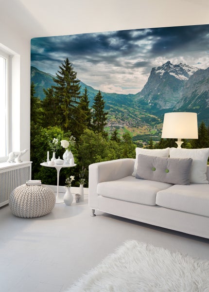 Modernes Wohnzimmer mit einer Fototapete eines Alpenpanoramas mit Bergen, Wald und Tal, kombiniert mit einem hellen Sofa und Dekoration.