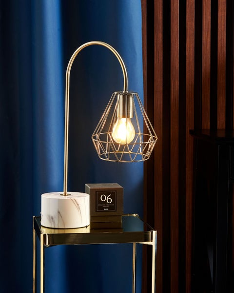 Dekorative Tischleuchte mit Marmorfuß und geometrischem Drahtschirm auf einem Beistelltisch.