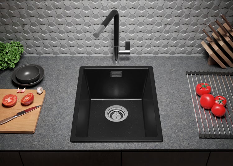 Schwarzes Spülbecken mit Abtropffläche, Armatur und Lebensmitteln auf einer Küchentheke.