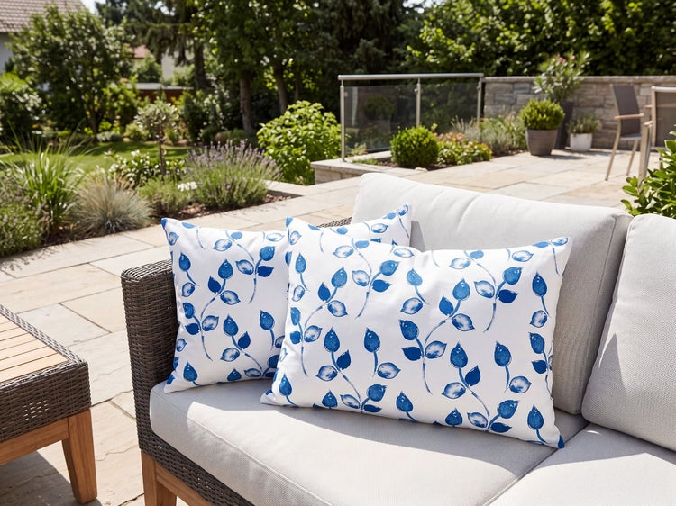Zwei quadratische Dekokissen mit blauem Blattmuster auf Gartenlounge auf Terrasse mit Blick in den Garten