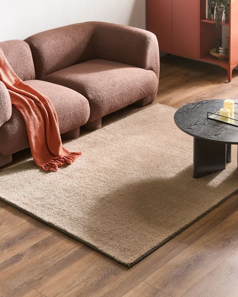 Rechteckiger, strukturierter Teppich auf Holzboden in einem hellen, gemütlichen Wohnzimmer mit geschwungenem Sofa und rundem Couchtisch.