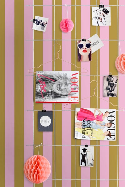 Gestreifte Tapete mit vertikalen Streifen in Rosa und Gold, dekoriert mit einem Gitter aus Metall, Zeitschriften und Papierkugeln.