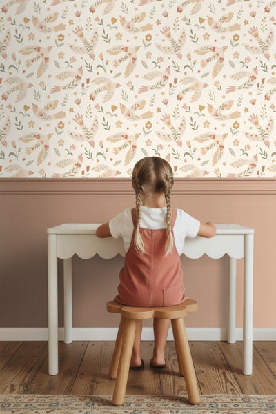 Mädchen sitzt an einem Schreibtisch vor einer Wand mit Vogelmuster-Tapete
