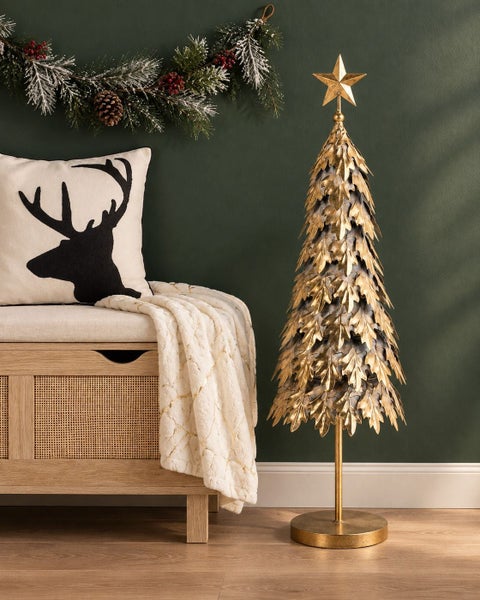 Dekorativer Weihnachtsbaum aus Metall im Blätterdesign mit Sternspitze neben einer Sitzbank mit Hirschkissen und Decke im Wohnbereich
