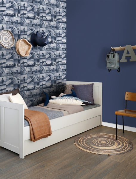 Ein Kinderzimmer mit einem weißen Bett, einer gemusterten Tapete und dekorativen Elementen.