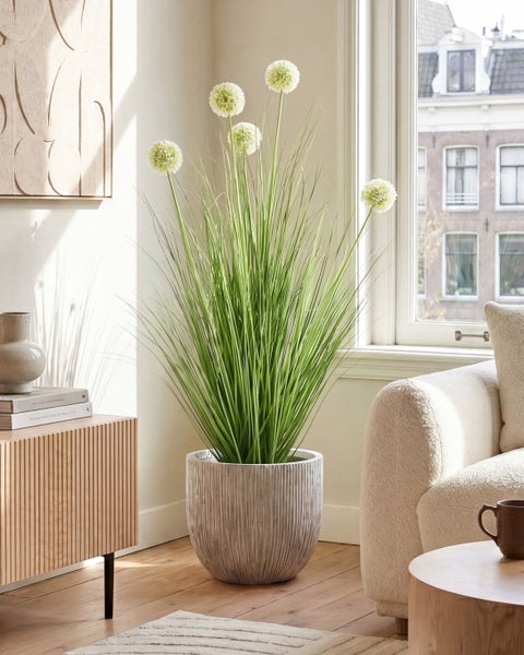 Künstliche Allium-Pflanze mit langen Gräsern und weißen Blütenköpfen in einem strukturierten grauen Topf in einem hellen Wohnzimmer.