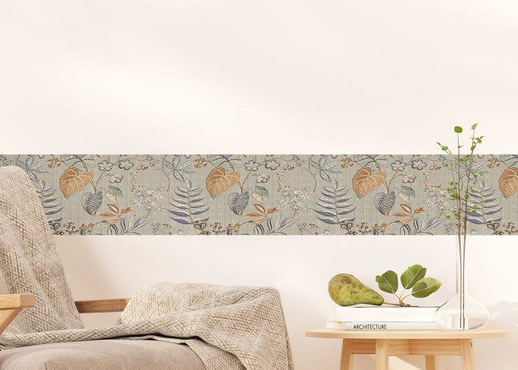 Tapetenbordüre mit botanischem Blatt- und Blumenmuster an einer Wand in einem Zimmer mit Sessel und Beistelltisch.