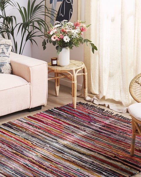 Hell eingerichtetes Wohnzimmer mit bunt gestreiftem Fleckerlteppich auf Holzboden, Cordsofa und Beistelltisch aus Bambus.